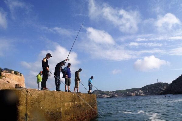 Un groupe de personnes pêchant le long d’une côte rocheuse, sous un ciel dégagé.