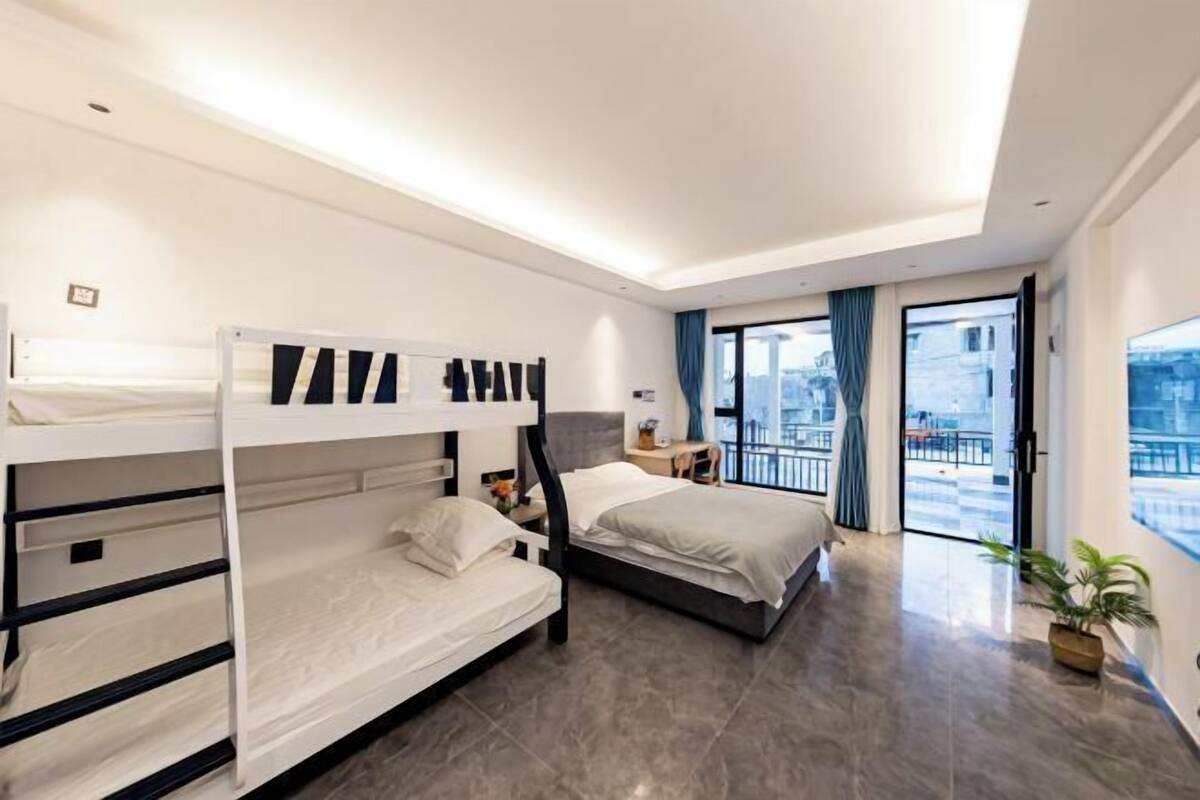 Una habitación de hotel moderna con literas, un ventanal con vistas a la ciudad, un balcón y una planta en maceta.