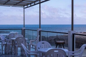 Un espace extérieur abrité, doté de chaises et de tables, offrant une vue sur l’océan.