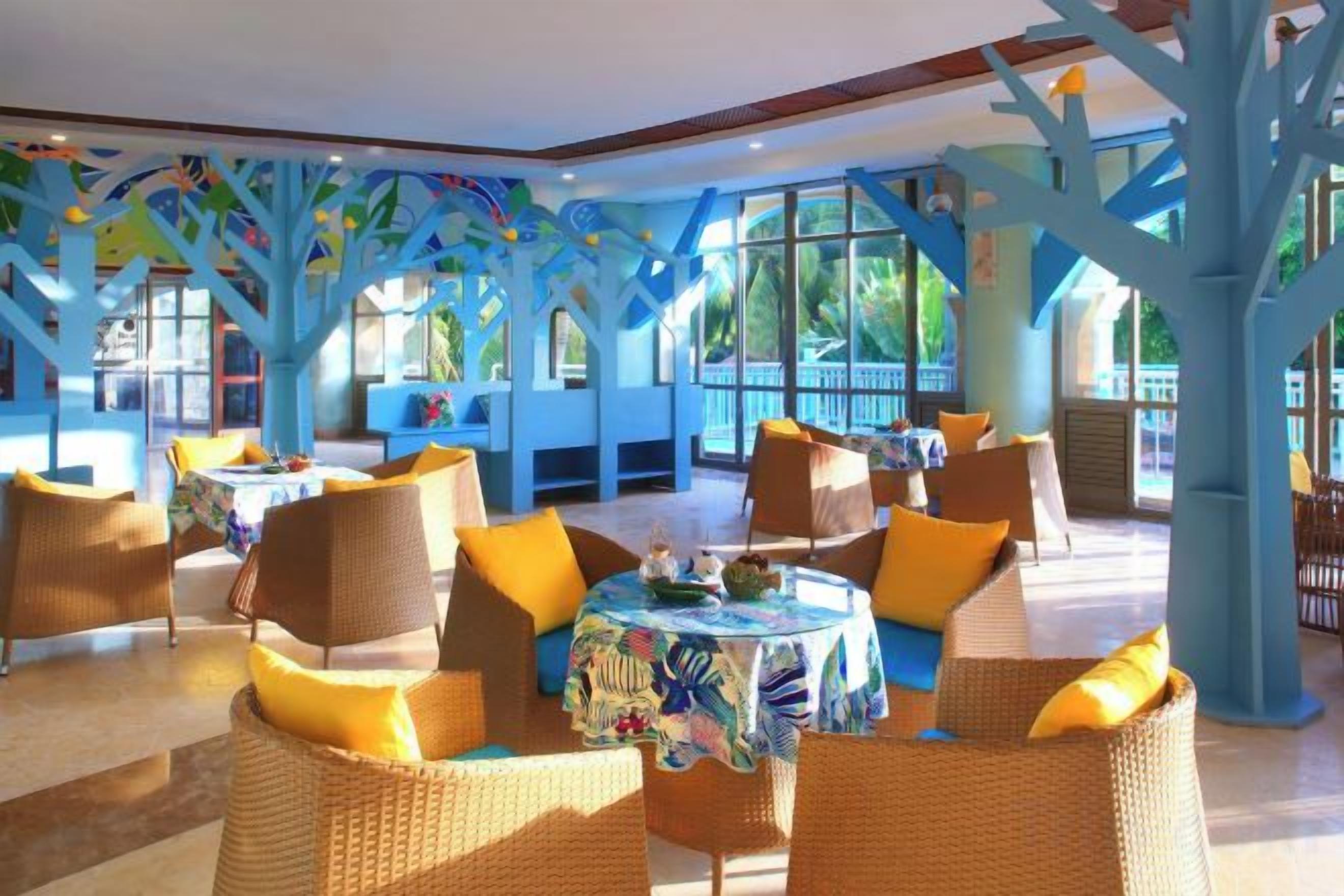 A spacious indoor area with wicker furniture and a colorful tablecloth, featuring large windows and a tree-like architectural design.