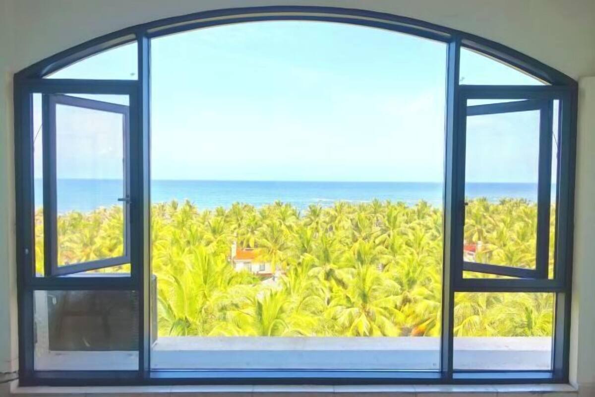 A room with a large arched window overlooking a tropical landscape with palm trees and a view of the ocean.
