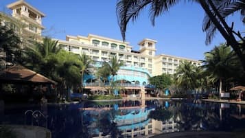 Un resort con una piscina grande, palmeras y un edificio de varios pisos con balcones.