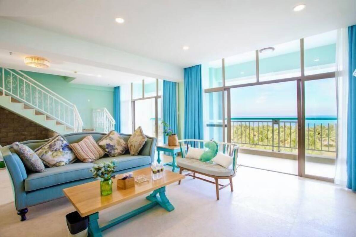 A spacious living area with a sofa, a coffee table, and a chair. There is a staircase leading to an upper level.