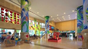 Eine geräumige Lobby mit hohen Decken, markanten Säulen und farbenfrohen Wandgemälden.
