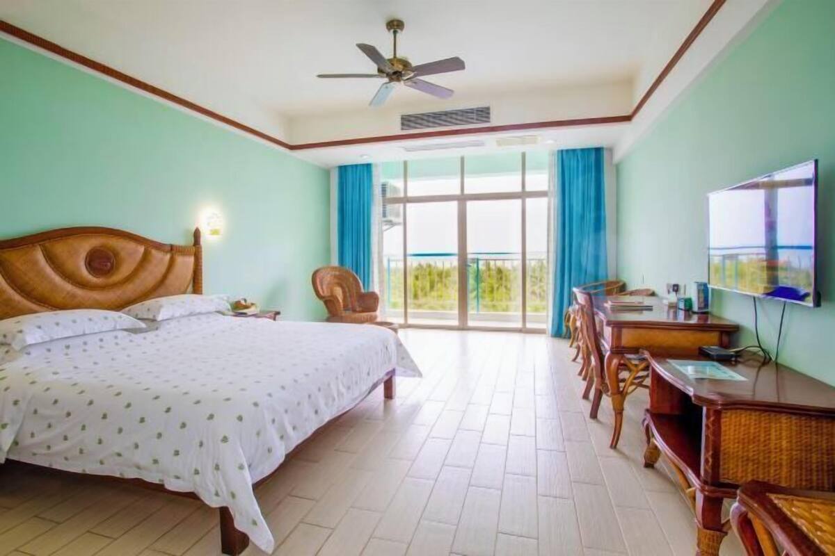 A hotel room with a bed, a desk, a chair, a television, and a balcony with a view.