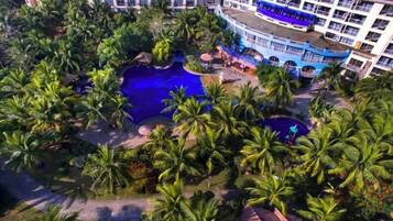 A resort with multiple swimming pools surrounded by palm trees, a blue bus, and a large building with balconies.