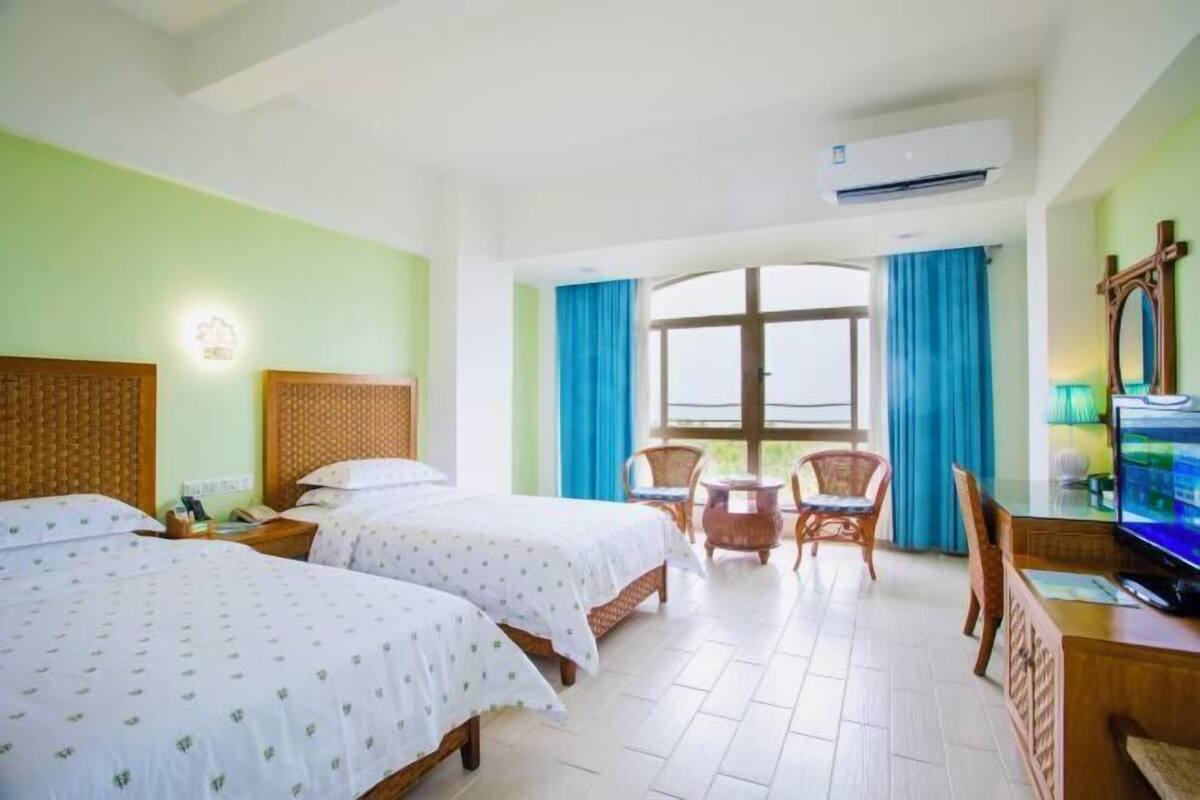 A hotel room with two beds, a dining area with chairs, a television, and an air conditioning unit.