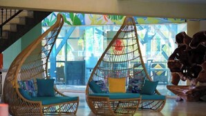 Ein modernes Interieur mit zwei Schaukelstühlen aus Rattan, blautönen Kissen, einer Treppe und einem farbenfrohen, abstrakten Wandbild.