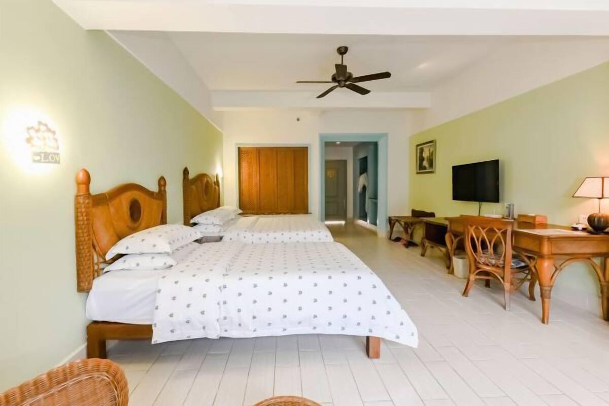A hotel room with a large bed, a desk with a chair, a television, and a ceiling fan.