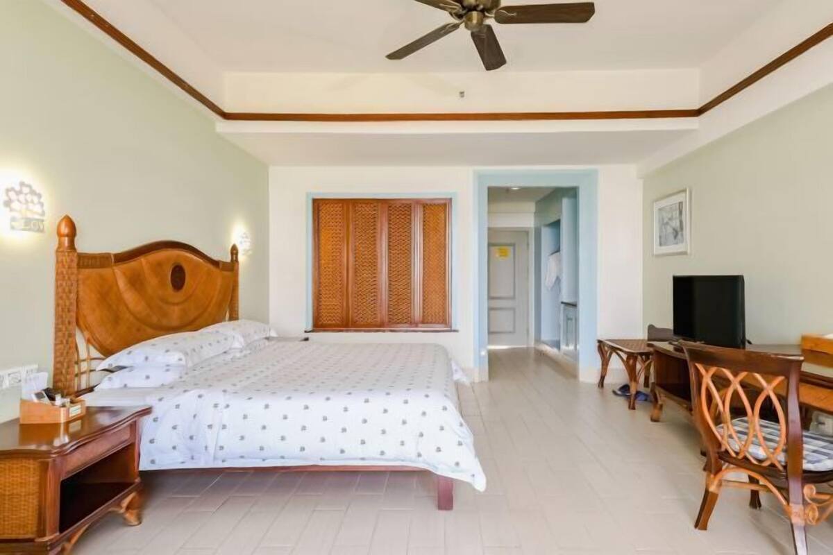 A hotel room with a bed, a desk, a chair, a television, and a ceiling fan.