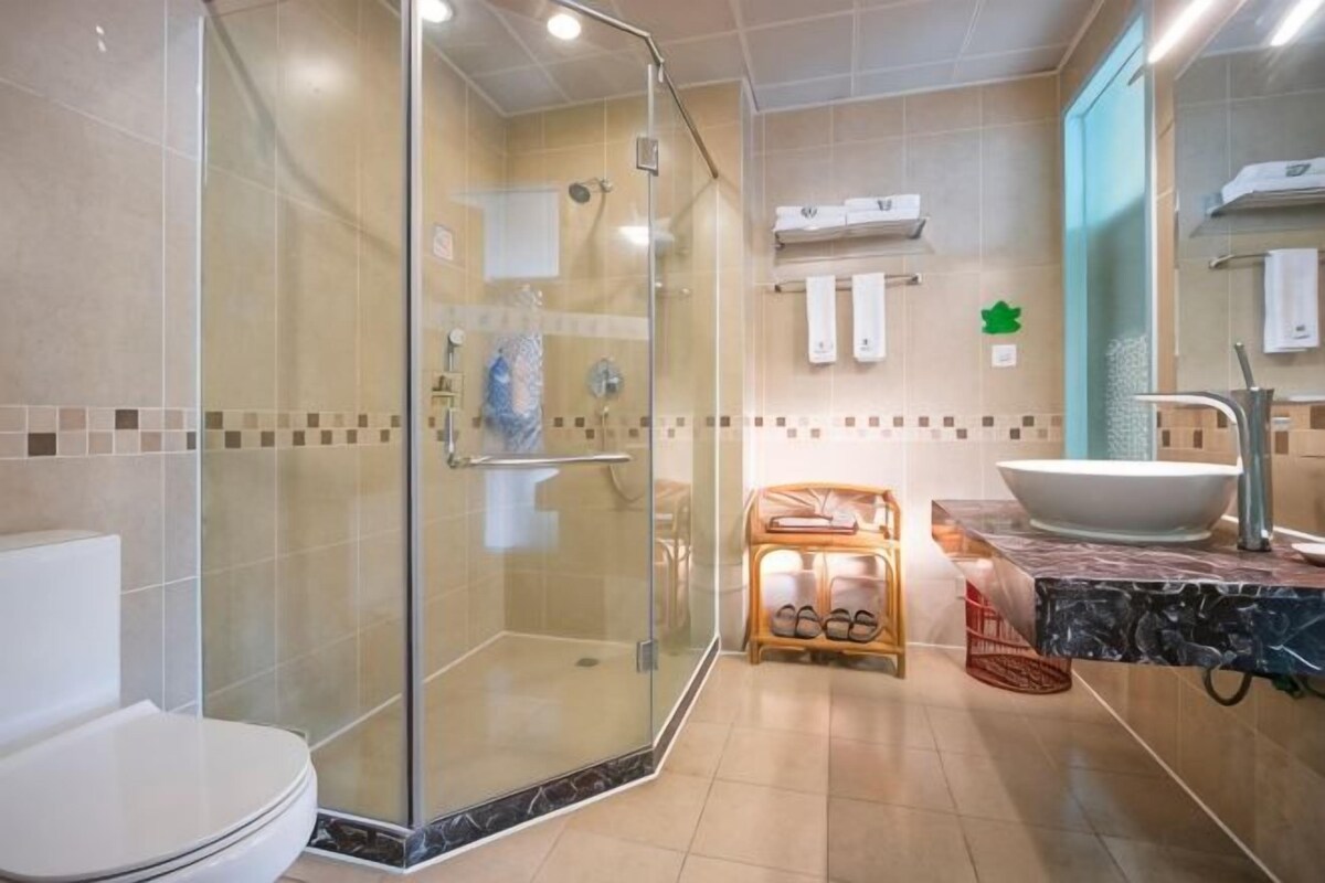 A bathroom with a glass-enclosed shower, a white toilet, a sink with a large basin, and a tiled floor.