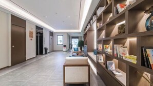 Eine moderne Hotelhalle mit einem langen Korridor, einer Sitzecke mit gepolsterten Bänken und einem Bücherregal mit Büchern und Dekoration.