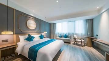 A modern hotel room with a large bed, bedside tables, a desk, and a seating area.