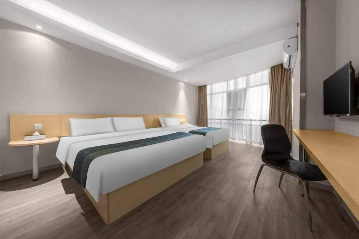 Een hotelkamer met twee bedden, een bureau, een stoel, een televisie en een raam met gordijnen.
