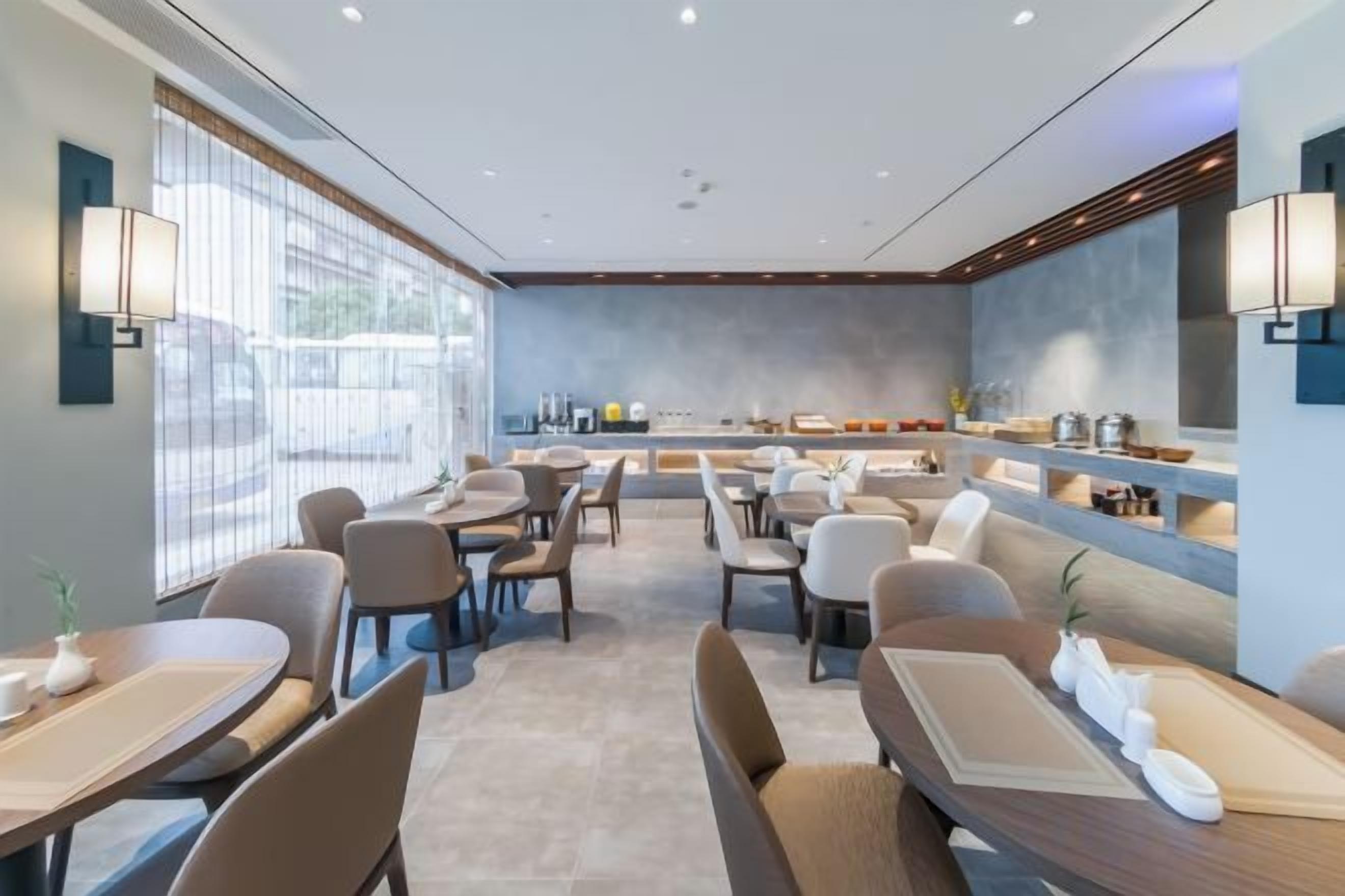 A modern dining area with multiple tables and chairs, a counter with a display, and large windows providing natural light.