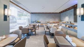 A modern dining area with multiple tables and chairs, a counter with a display, and large windows providing natural light.