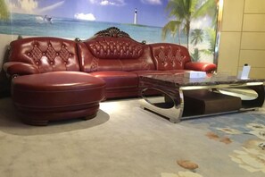 Un sofá de cuero rojo con un reposapiés a juego y una mesa de centro de vidrio en una habitación con un mural de una escena playera.