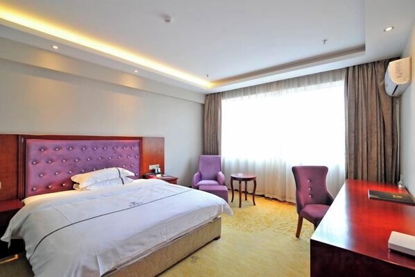 Habitación de hotel con una cama grande, dos sillas, un escritorio y una ventana con cortinas.