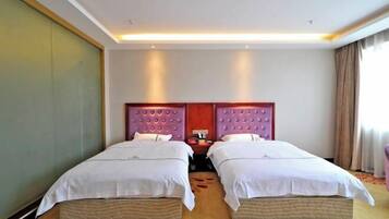 A hotel room with two single beds, a wooden floor, a large mirror, and a red accent wall.