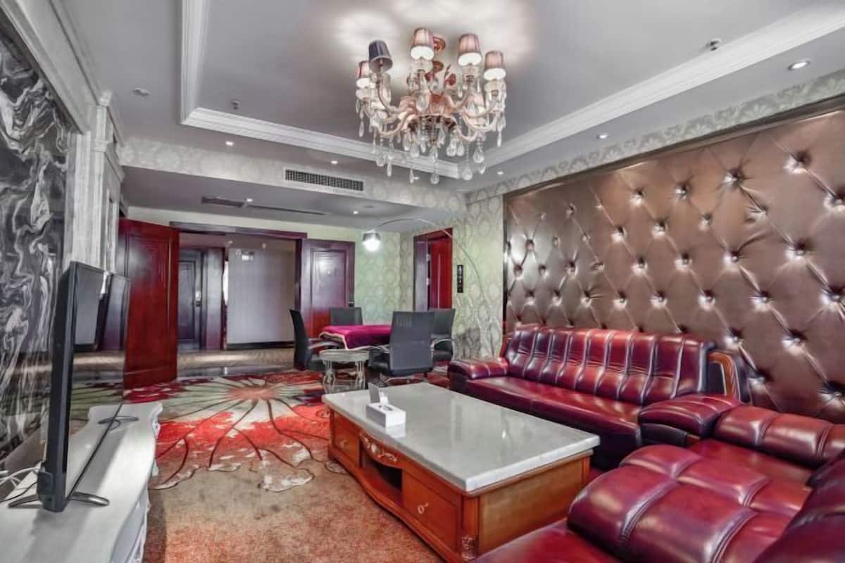 A spacious living area with a large tufted sofa, a television, and a chandelier.