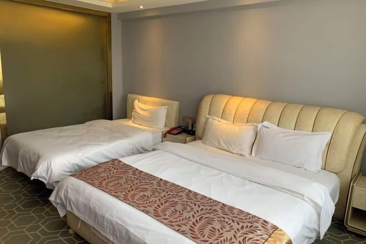 A hotel room with two beds, a large bed with a headboard, and a smaller bed.