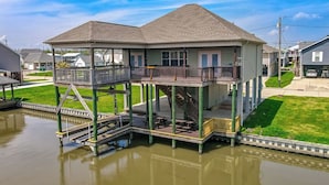 A two-story waterfront house with a balcony, a covered patio, and a dock extending into the water. - New For 2025 - Waterfront Bayou Retreat: 25 Min to NOLA. (Barataria)