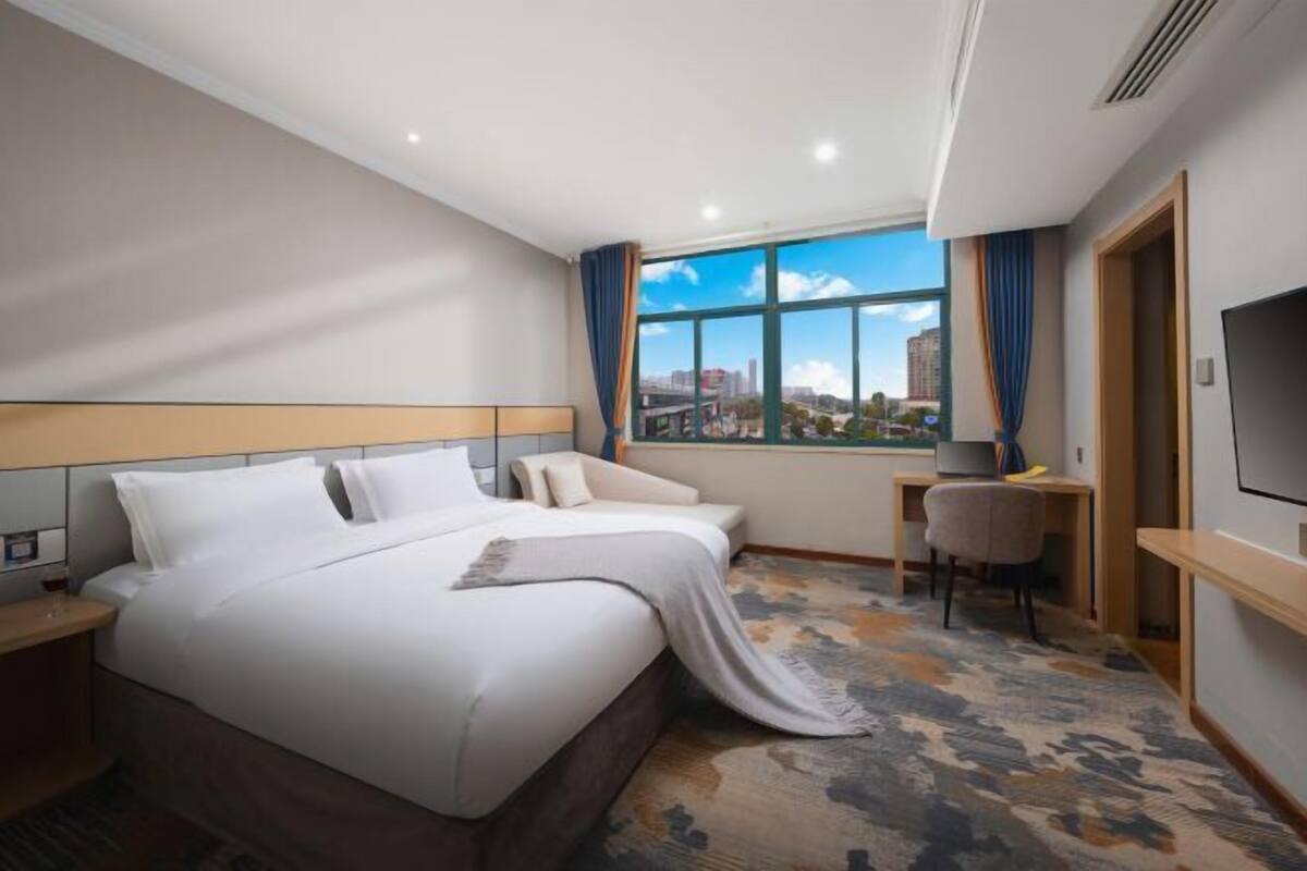 A hotel room with a large bed, a desk, a chair, and a TV.