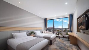 Habitación de hotel con dos camas, un escritorio, una silla, un televisor y un ventanal con vistas a la ciudad.