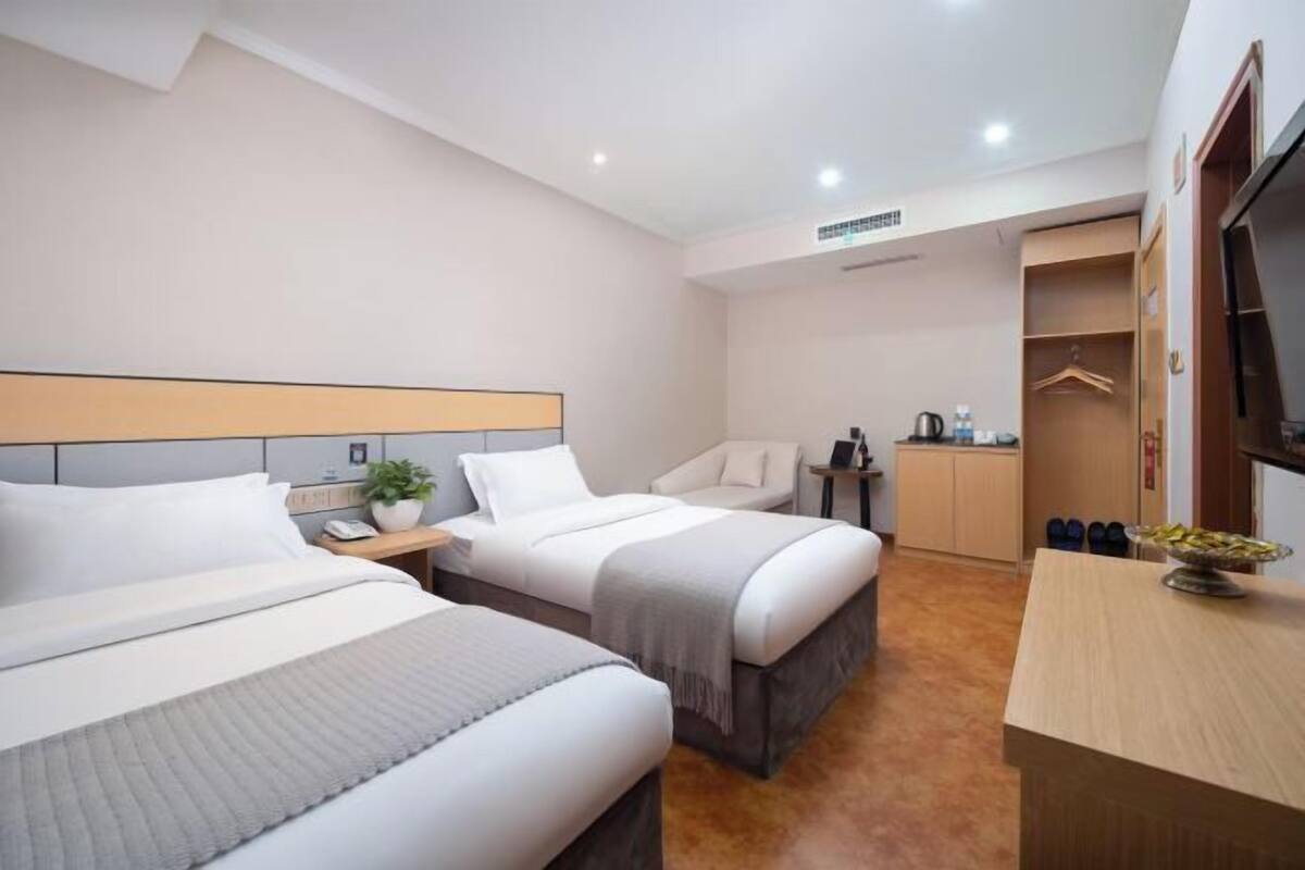 A hotel room with two beds, a desk, a wardrobe, and a TV.