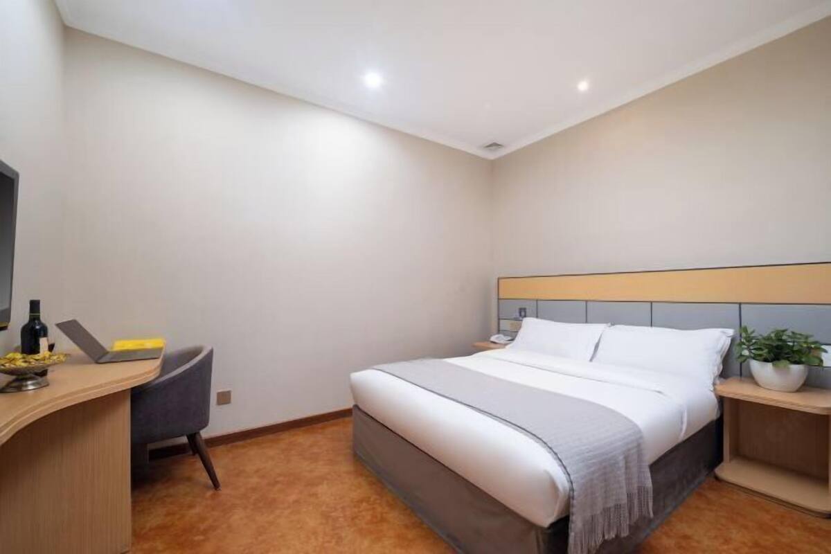A hotel room with a bed, desk, chair, and a small potted plant.