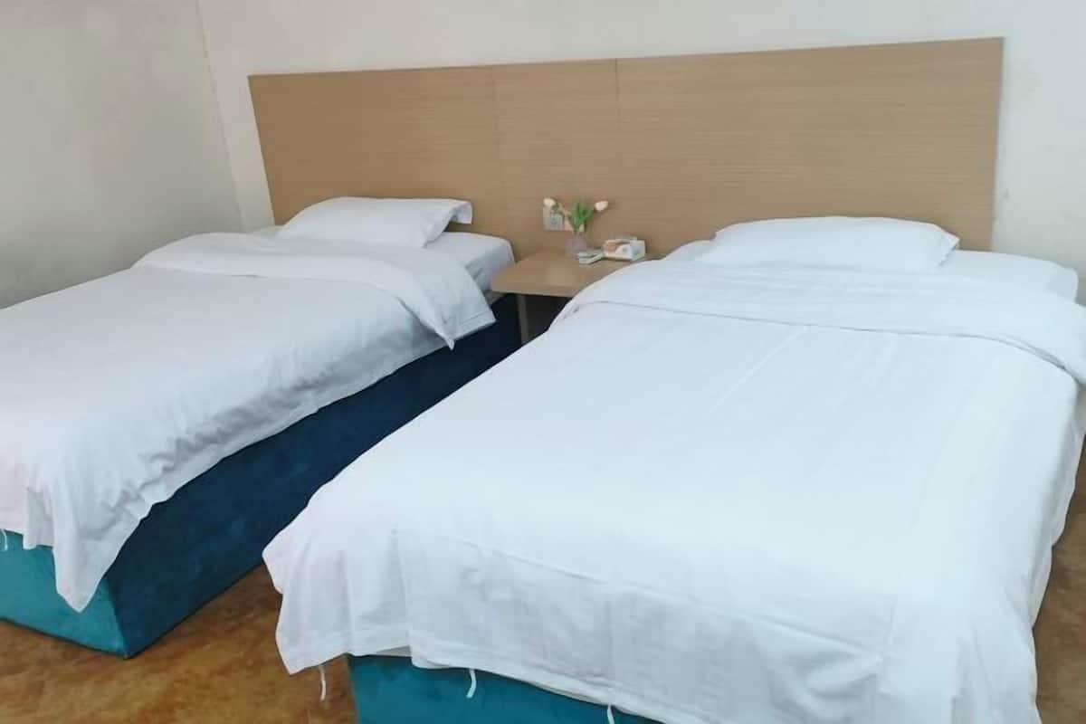 A hotel room with two single beds, a wooden headboard, a small table with a vase of flowers, and a teal-colored bed base.