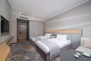 Habitación de hotel con dos camas, un televisor, una mesita con teteras y un sofá.