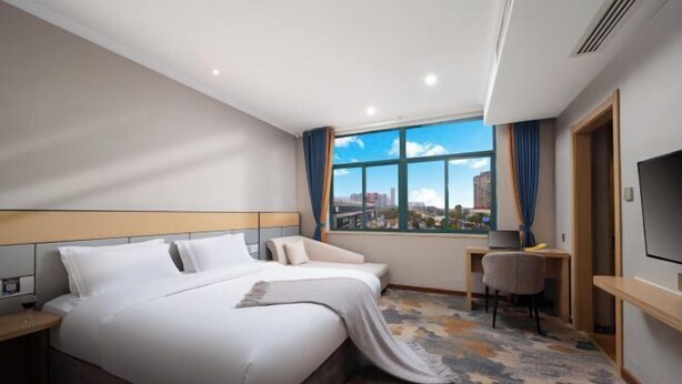 Habitación de hotel con una cama grande, un escritorio, una silla, un televisor y una ventana con vistas a la ciudad.
