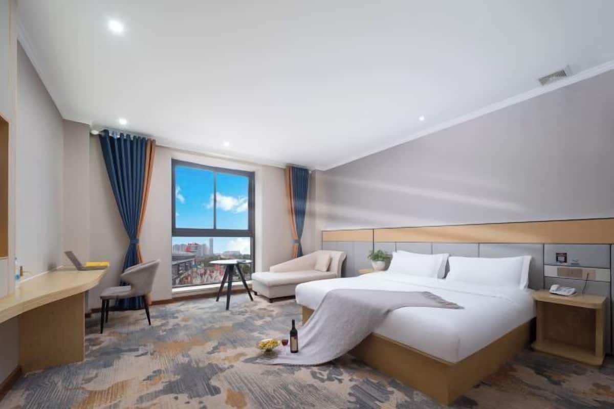 A hotel room with a bed, a desk, a chair, a small table, a window with curtains, and a view.