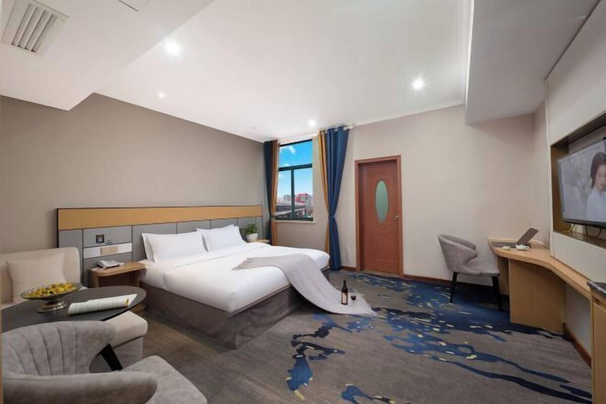 A hotel room with a bed, a desk, a chair, a TV, and a window with curtains.