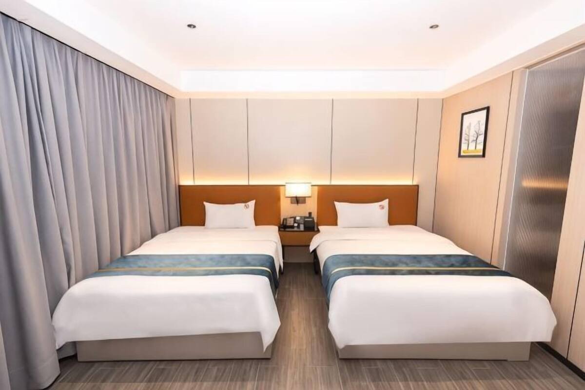 A hotel room with two beds, a nightstand, a lamp, a wardrobe, and a framed picture on the wall.
