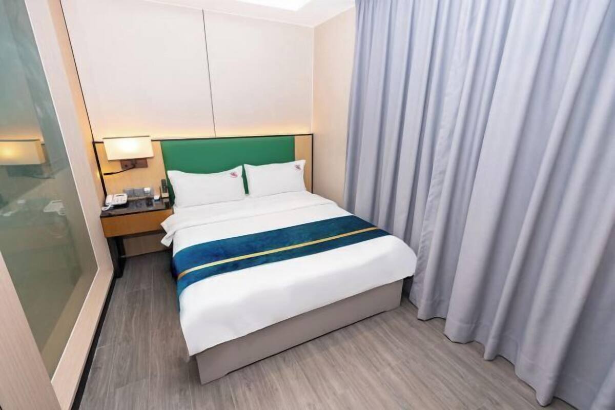 A hotel room with a bed, a nightstand, a lamp, and a curtain.