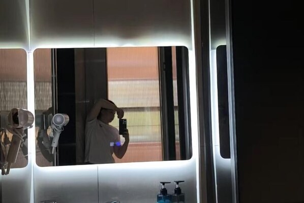 A bathroom with a mirror, a hairdryer, and two bottles of liquid soap. - Foshan Shunde Weierke Hotel (Lunjiao Recreation Center) (Foshan)