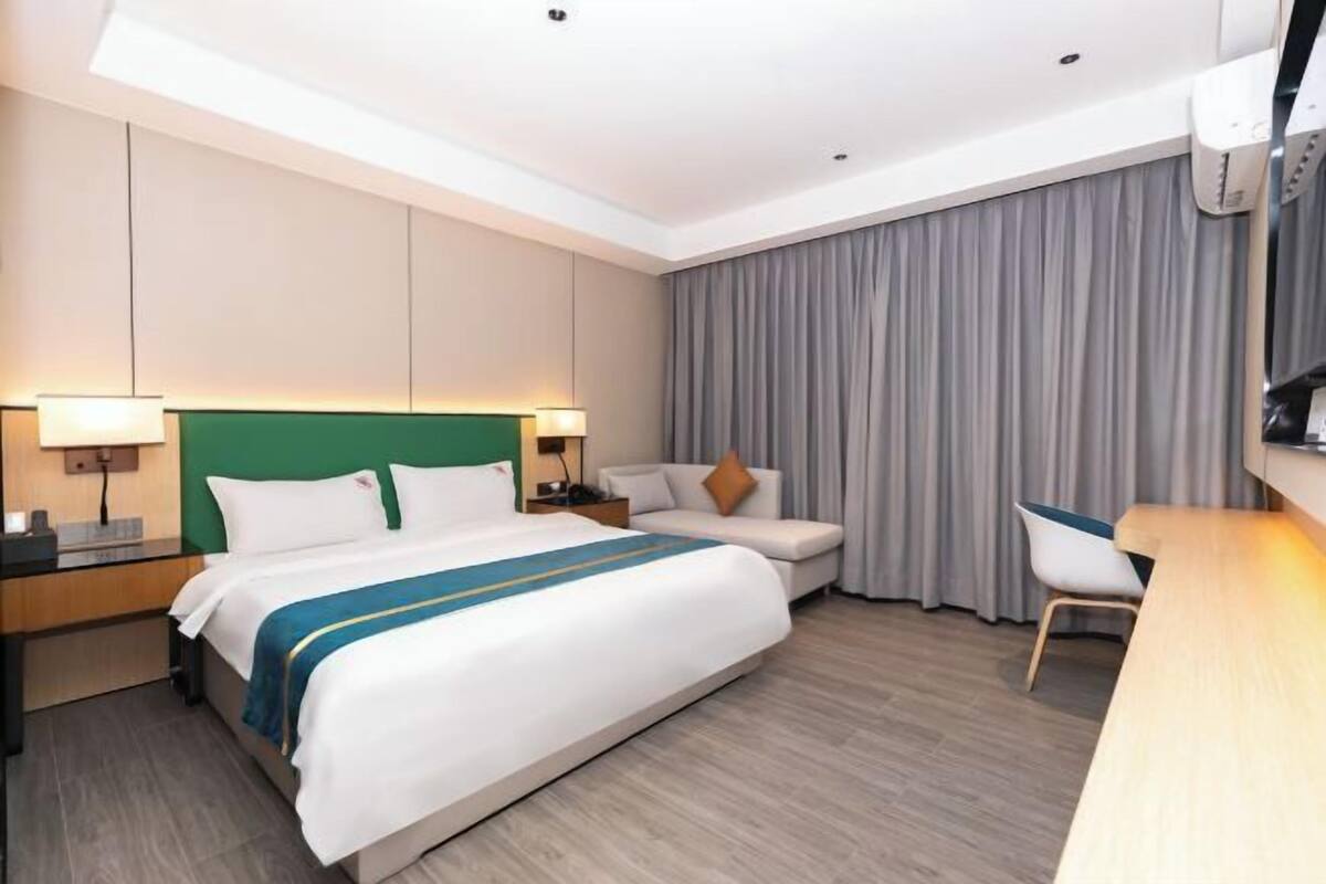 A hotel room with a bed, a desk, a chair, a nightstand, and a large window with curtains.