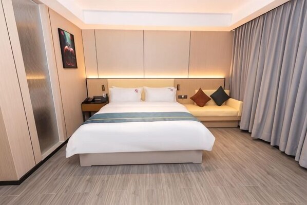 A hotel room with a large bed, a bedside table, a nightstand, a sofa, and a curtain.