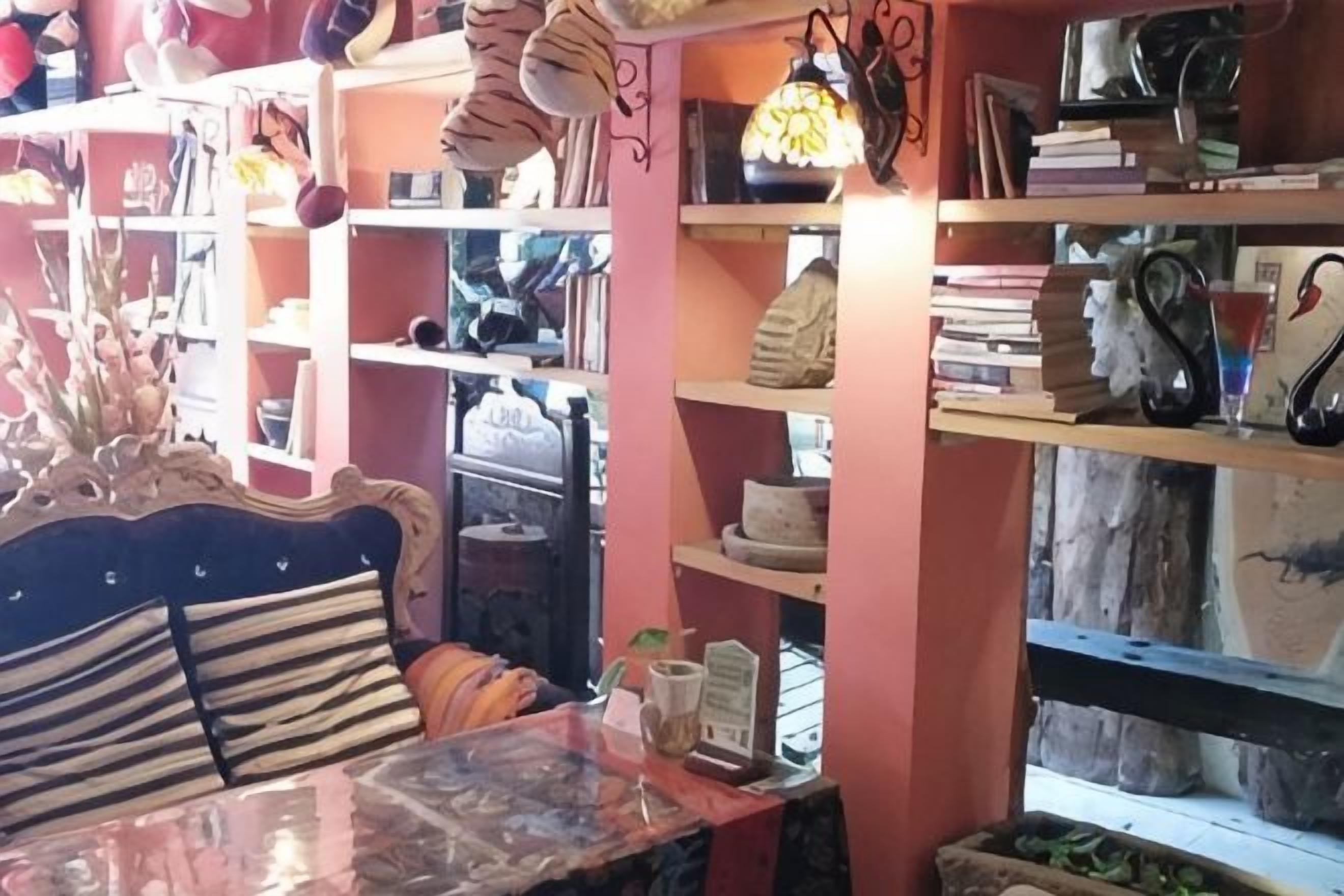Quarto com cama, uma mesa e estantes cheias de livros e objetos decorativos.
