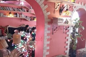 A room with a pink wall, a bookshelf, a plant, and a decorative light fixture. - Banduo Youlian Hostel (Shanghai)