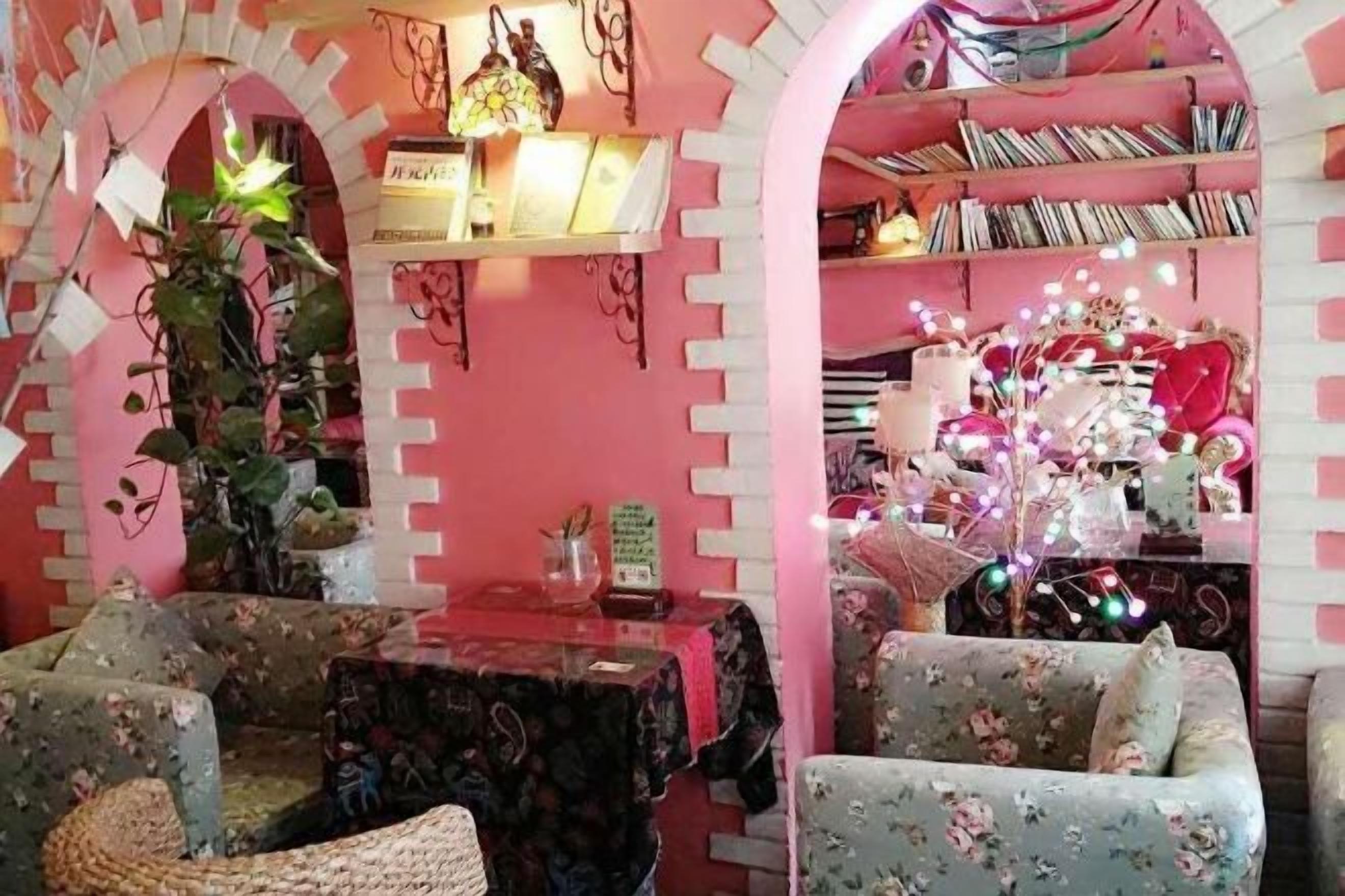 Um quarto aconchegante com parede rosa, uma estante, uma mesa e duas cadeiras.