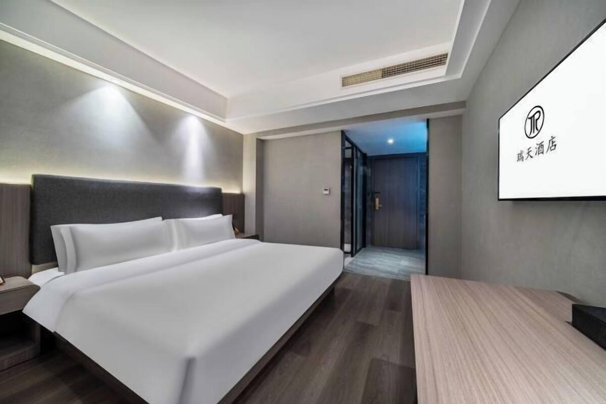 A modern hotel room with a large bed, a desk, and a view of the hallway.