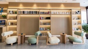 Un moderno vestíbulo de hotel con mostrador de recepción, zona de estar y estanterías.