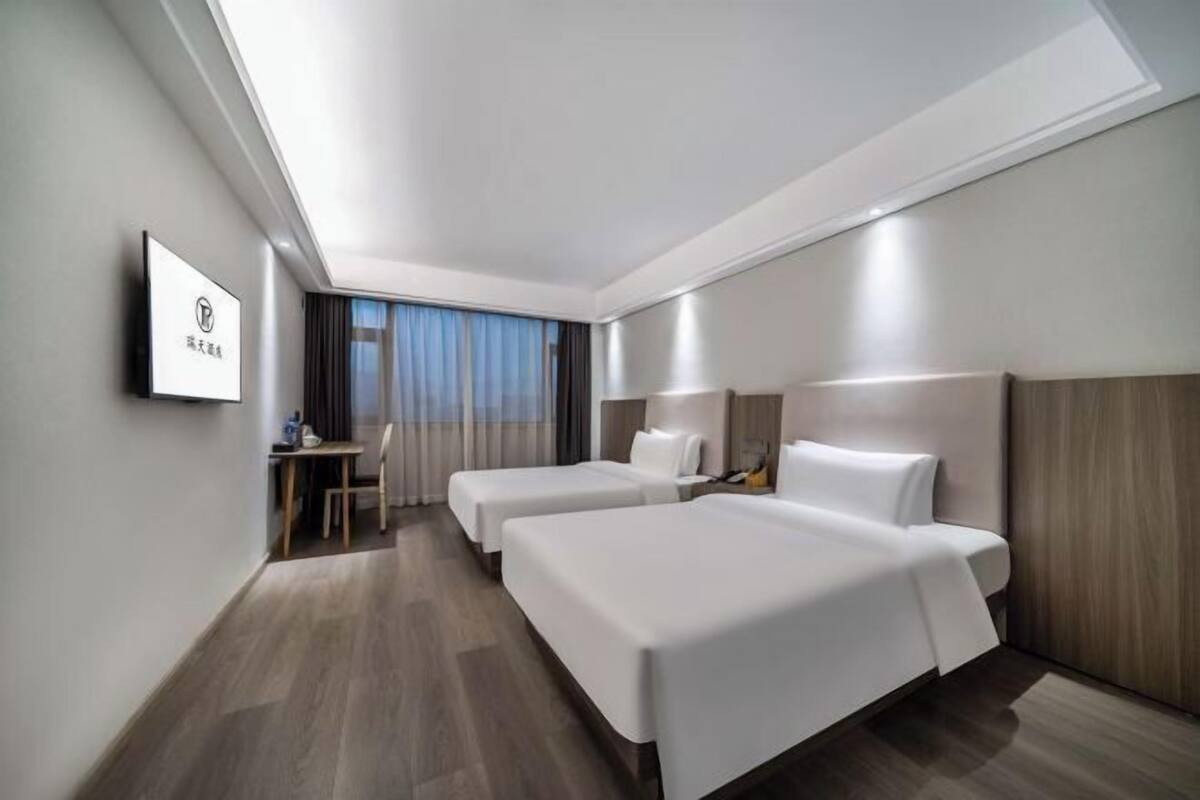 A hotel room with two beds, a desk, a chair, and a TV on the wall.