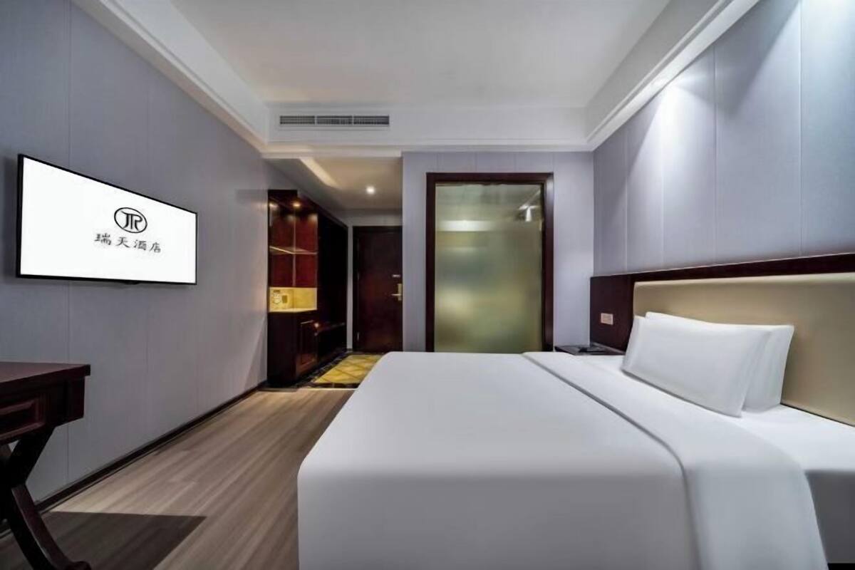 A hotel room with a bed, a desk, a TV, and a door leading to a hallway.