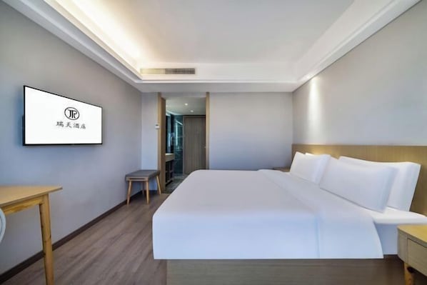 Habitación de hotel con una cama grande, una mesita pequeña, una silla y un televisor montado en la pared.