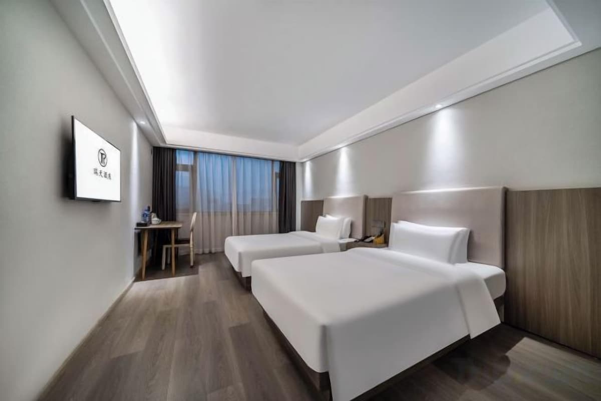 Habitación de hotel con dos camas, un escritorio y televisión.