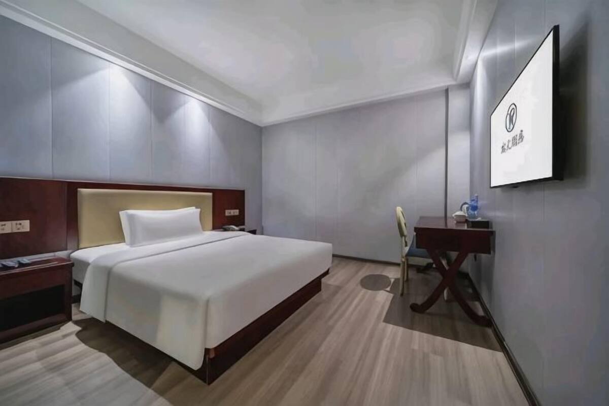 A hotel room with a bed, bedside table, lamp, and a TV mounted on the wall.